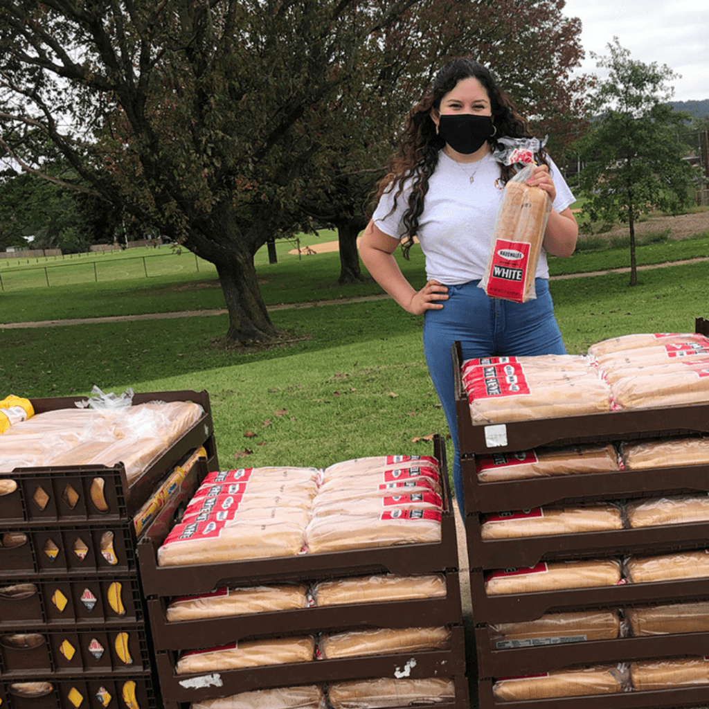 a woman wearing a face mask standing next to stacks of bread