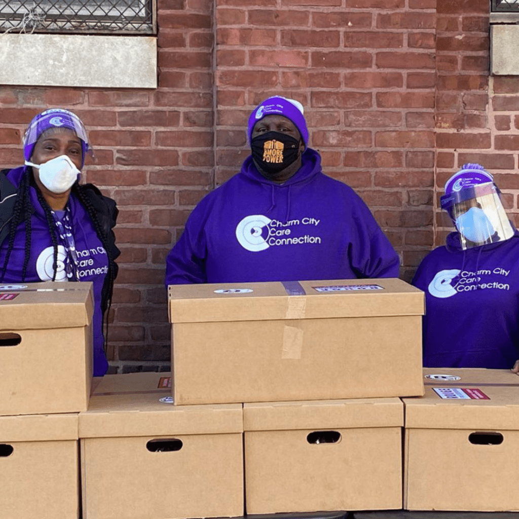three people in purple shirts and masks standing behind boxes