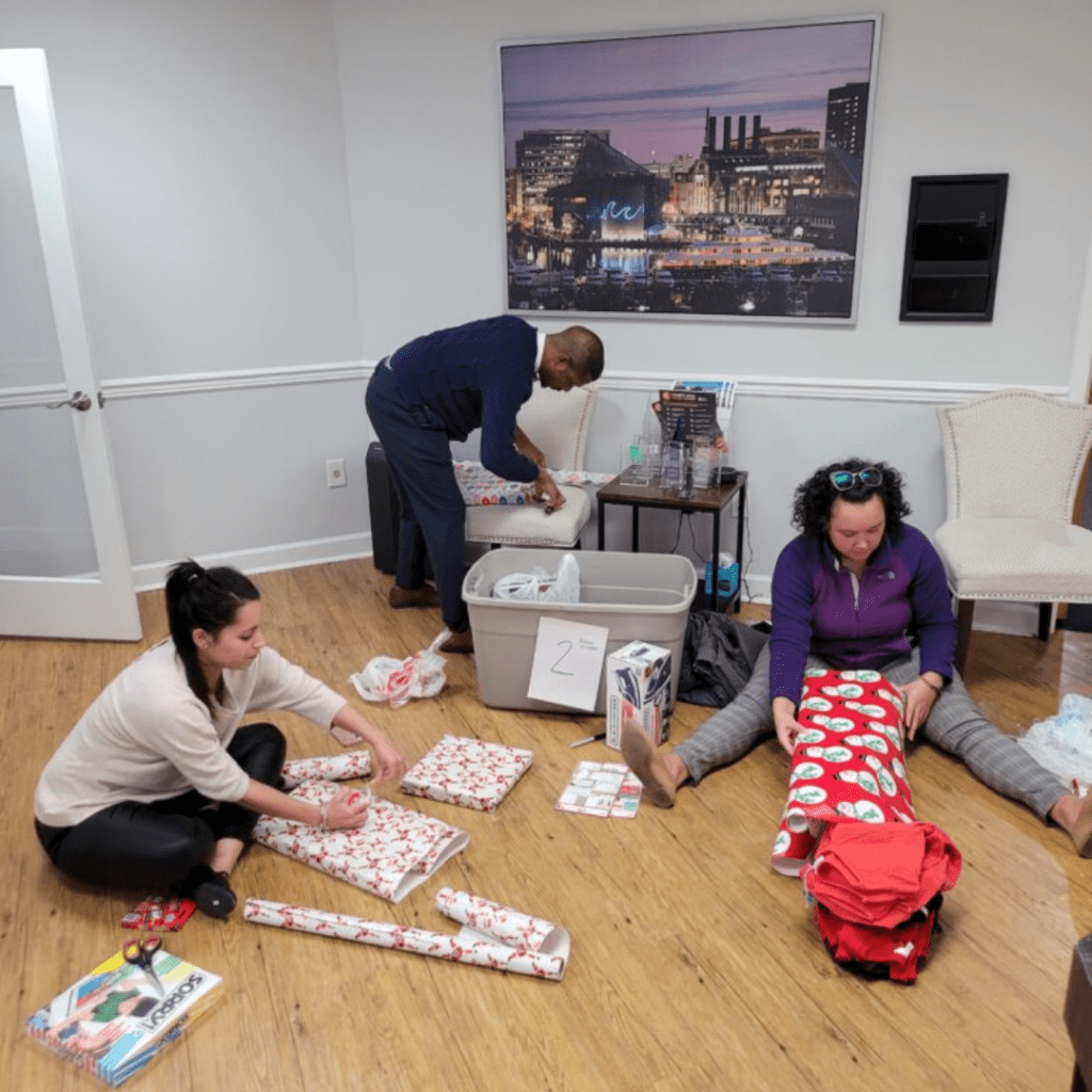 three people opening presents on the floor in an office