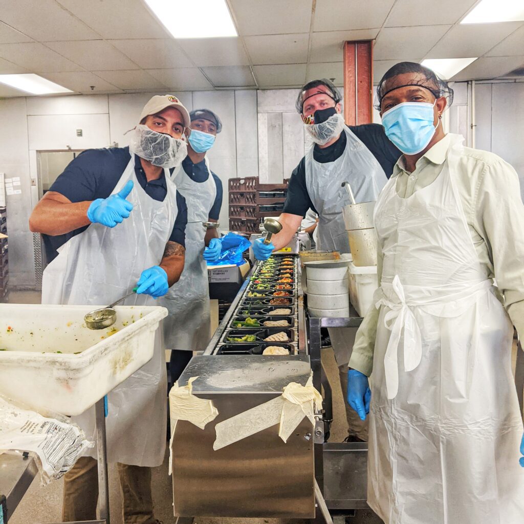 four men in white aprons and masks preparing food